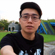 Toyz is standing in a parking lot near a green field.
